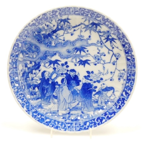 A Japanese blue and white porcelain plate, decorated with figures beneath a flowering tree, bearing four character mark, 21.5cm diameter.