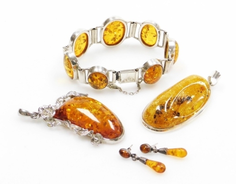 A group of silver and amber jewellery, comprising a silver and amber pendant, 7cm high, another in silver plated frame with heavy floral detailing, 6cm high, a pair of silver and amber drop earrings, and a silver and oval amber set bracelet, 20cm long ove