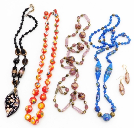 A group of Murano style glass beaded necklaces, comprising a red cane design necklace, 50cm long, a blue applied floral design necklace, 80cm long, a further purple example with paste set stone and matching earrings, and a black and gold glitter example. 