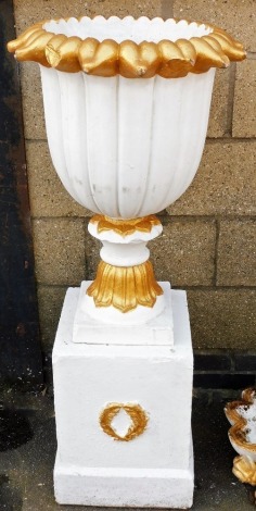 A composition garden urn, with a stylised leaf border and fluted sides on a square base, the associated plinth decorated with wreaths, later painted white and gilt, 118cm high overall.