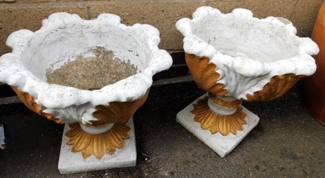 A pair of composition garden urns, each cast with a bold design of leaves on a square base, later painted white and gilt, 44cm high, 48cm wide.