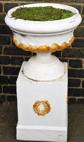 A composition garden urn, of plain form with part fluted body on a tapering base with associated plinth decorated with wreaths, later painted white and gilt, 95cm high overall.