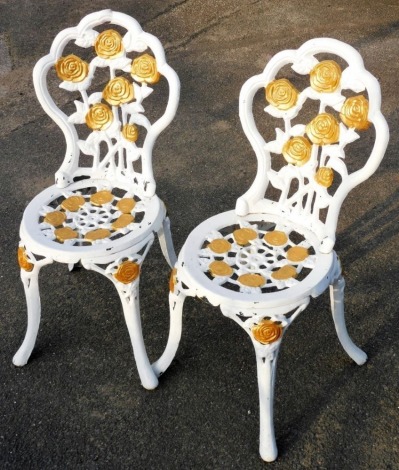 A pair of gilt and white painted aluminium garden chairs, each decorated with flowers and leaves on cabriole legs.