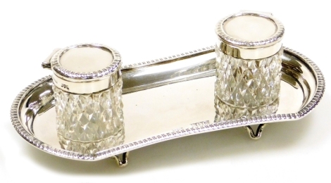 A Victorian silver desk stand, with two cut glass and silver mounted ink pots, the stand with an impressed edge raised on four feet, John Grinsell & Sons, London 1899, the base 18cm wide, weighable silver 4oz.