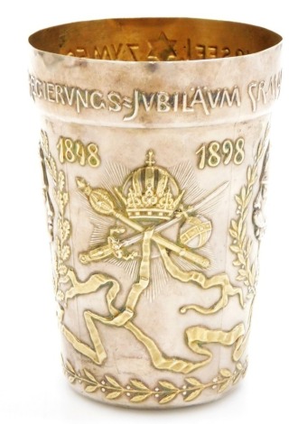 A late 19thC Austrian gilt metal commemorative beaker, for the Golden Jubilee of Emperor Franz Josef I of Austria 1848-98, embossed with bust portraits of the Emperor at the two dates, within laurel wreaths, flanking the royal regalia, verso 'Gott erhalte