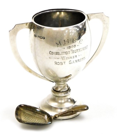 A George V silver two handled trophy, engraved 'MHBC 1940 Consolation Tournament Winner Robert Garrett,' Sheffield 1934, 10cm high, and a George IV silver caddy spoon, with bright cut decoration to the bowl and handle, Birmingham 1822, 2¾oz.