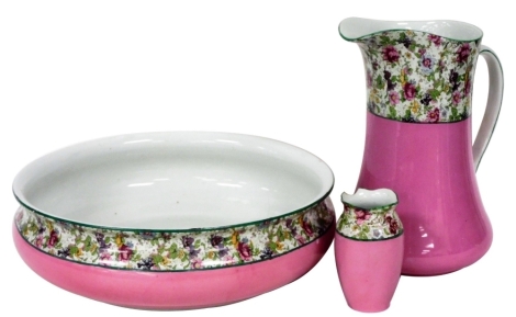 An Empire Works pottery part set, each printed with a sheet design of flowers, against a pink ground, printed marks, comprising wash jug, bowl and toothbrush holder. (3)