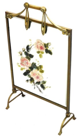 An early 20thC brass fire guard, the bevelled mirror centre painted with roses, the frame applied with stylised ribbons, swags, etc., on pierced feet, 79cm high, 46cm wide.