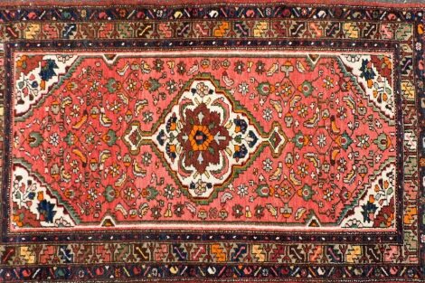 A 20thC Iranian rug, with an outer field of geometric border, in bright colours predominantly in red and green, the inner section with a geometric floral pattern, 210cm x 147cm.