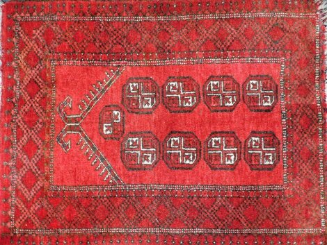 A Beluchi type prayer rug, with a design of medallions, on a deep red ground with one wide border, 110cm x 84cm.