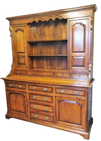 A Georgian style oak and mahogany cross banded dresser, the outswept pediment and dental moulding, above a carved frieze and two central plate racks, flanked by a pair of carved panel doors, over five short drawers, the base with two drawers over a pair o