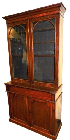 A Victorian mahogany bookcase, with out swept pediment, raised above two arched glass doors opening to reveal shelves, the sub section with drawer raised above two cupboard with fielded panels, on a plinth base, 120cm high, 114cm, 49cm deep.