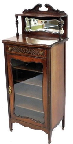 An Edwardian mahogany music cabinet, the raised back with swan neck pediment above a shelf, with moulded edge and a bevelled mirror plate, the serpentine fronted base with a moulded edge above a blind fret carved frieze and a glazed door, on square taperi