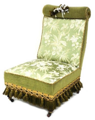 A Victorian mahogany nursing chair, upholstered in green floral fabric, with a tasselled border, on turned legs with ceramic castors.