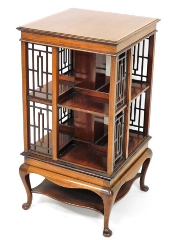 An Edwardian mahogany revolving bookcase, with satinwood cross banding, of square two tier form, with eight compartments and fret work panelling, raised on a table base over four cabriole legs, united by an under tier, 86cm high, 46cm wide.