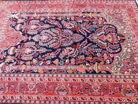 An Iranian carpet, with an outer field of floral geometric pattern, predominantly in red and blue, 295cm X 195cm.