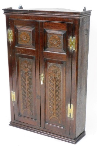 A principally 18thC oak hanging corner cupboard, of large proportion, the fitted interior flanked by two later carved doors and a plain moulded base, 116cm high, 82cm wide, 56cm deep.