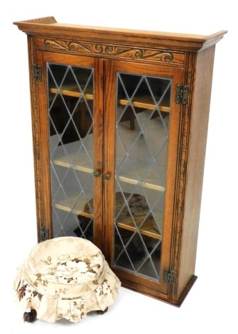 An oak Old Charm display cabinet, the top with a moulded cornice, with carved top, and two leaded glazed doors, 110cm high, and a 19thC walnut footstool, raised on three scroll cast legs, 36cm diameter,