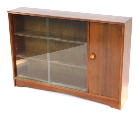 A mid century mahogany low bookcase, with two sliding glass doors, above three shelves with single cupboard door, 85cm high, 121cm wide, 24cm deep.