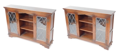 A pair of Old Charm oak cabinets, with two astragal glazed doors and central bookshelf section, on bracket feet, 83cm high, 121cm wide, 28cm deep.