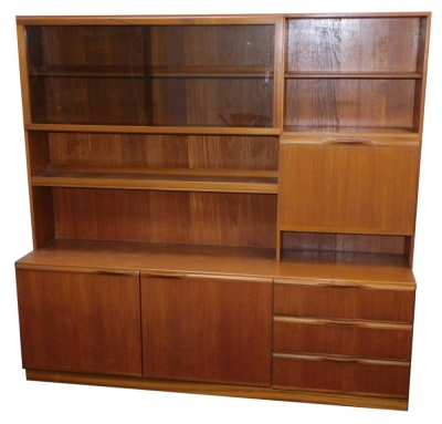 A mid century teak wall unit, with sliding two shelved bookshelf top section, with open bookcase, cocktail cabinet above sideboard with three doors, 170cm high, 179cm wide, 46cm deep.