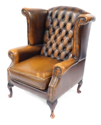 A brown leather Chesterfield wingback armchair, with button back and stud detailing, on out splayed mahogany legs, 110cm high, 90cm wide, 85cm deep. The upholstery in this lot does not comply with the 1988 (Fire & Fire Furnishing) Regulations, unless sold