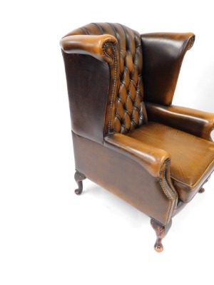 A brown leather Chesterfield wingback armchair, with button back and stud detailing, on out splayed mahogany legs, 110cm high, 90cm wide, 85cm deep. The upholstery in this lot does not comply with the 1988 (Fire & Fire Furnishing) Regulations, unless sold - 3