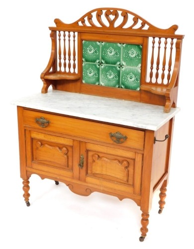 A Victorian washstand, with a leaf carved pediment over a six green tile floral splash back, flanked by spindles and shaped shelves, the marble top over a long drawer and panelled doors, raised on turned legs, on castors, 133cm high, 99cm wide, 46.5cm dee
