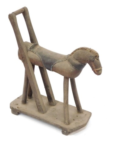 A vintage child's wooden pull along toy horse, with leather saddle on a wooden base, 46cm wide.