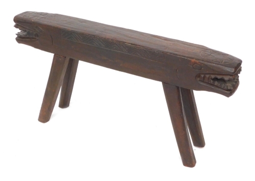 An African wooden two seated stool, the seat carved as a double headed crocodile, 98cm wide.