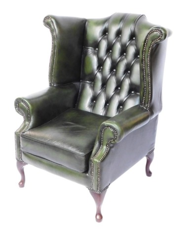 A green leather Chesterfield wingback armchair, the button back with single seat and studded upholstery on out splayed mahogany legs, 101cm high, 80cm wide, 62cm deep.