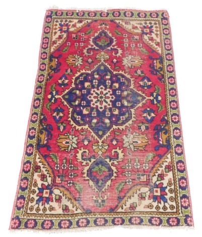 A Persian rug, with a central medallion in blue, surrounded by a meandering design of flowers, on a red ground, with cream spandrels, and one narrow border, 150cm x 100cm. (AF)