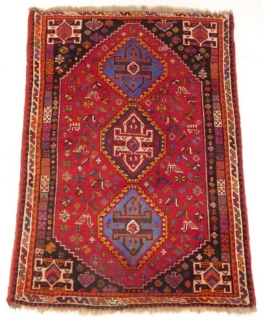 A Persian rug, with three lozenge shaped multicoloured medallions, on a ref ground decorated with birds and animals within multiple borders, 166cm x 112cm.