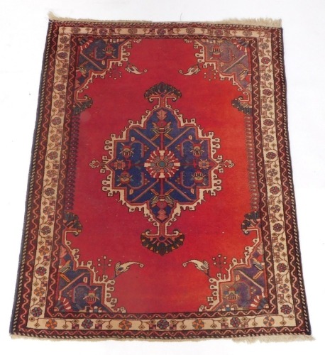 A Persian rug, with a central shaped medallion in blue, on a red ground, with purple spandrels within multiple borders, 110cm x 148cm.