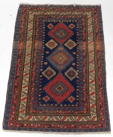 A Persian Kazak type rug, with three geometric medallions in deep orange and pale blue, on a blue ground with multiple borders, 127cm x 190cm.