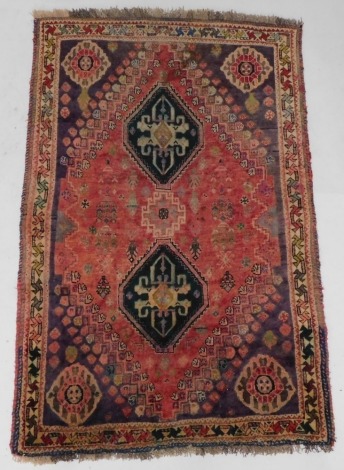 A Persian rug, with two lozenge shaped medallions, on a red ground with purple geometric spandrels, within multiple borders, 180cm x 110cm.