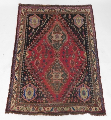 A Persian rug, with two lozenge shaped medallions, in green on a red ground with black spandrels decorated with flowers, etc, within three borders, 188cm x 121cm.