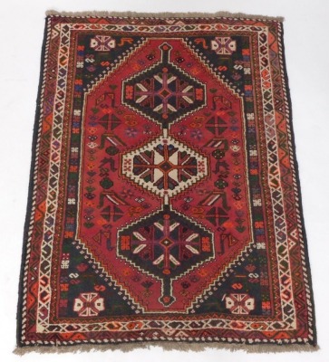 A Persian rug, with a central medallion in cream, navy, red, etc, on a red ground with spandrels, surrounded by multiple borders, 172cm x 122cm.