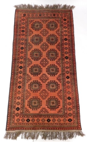 An Afghan Belouch rug, with a design of medallions and lozenges, on a pale red ground with multiple borders, 218cm x 100cm.