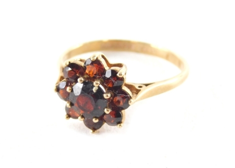 A 9ct gold garnet cluster ring, with central faceted stone surrounded by eight smaller stones, each in a raised basket claw setting, ring size U, 3g all in.