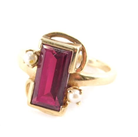 A ruby and seed pearl dress ring, the rectangular cut ruby in rub over setting with two cultured pearl surrounds, on a yellow metal band, stamped 10K, ring size L½, 3.8g all in, boxed.