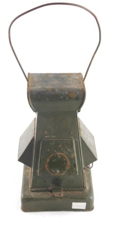 An early 20thC army metal lantern, with red glass centre and slanted shades, on a square base with swing handle, 43cm high.