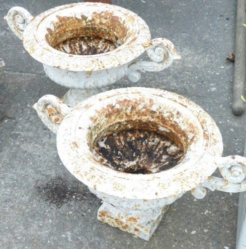 A pair of cast iron two handled urns, each with part fluted decoration, 30cm high, 57cm wide.