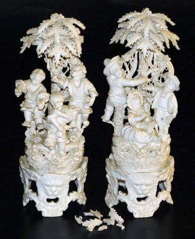 A pair of Continental white glazed biscuit figure groups on stands, each modelled with three boy figures on a naturalistic base with a tree and vine bocage, the stand moulded with repeating lion's head masks and rococo scrolls, blue crown and N mark, 38cm