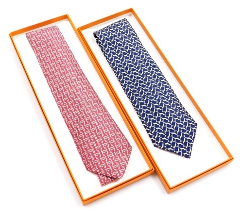Two Hermes silk ties, comprising a red tie with linked design, and a blue tie with horse bit link design, both boxed.