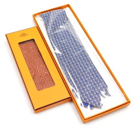 Two Hermes silk ties, comprising a blue tie with link design, and a red geometric pattern tie, both boxed.