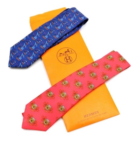 Two Hermes silk ties, comprising a blue tie with sailing boat design, and a red tie decorated with drums, contained in a Hermes sleeve case.