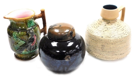 Three items of pottery, comprising a majolica jug, relief decorated with a bird on branch, 24cm high, an Oriental brown and black layers jar and cover, four character impressed mark to underside, 22cm high, and a West German jug, with angular handle and r