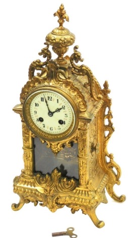 A French cast brass mantel clock, the domed top with a fleur de lis finial and applied with two dragon, with a cream enamel clock face and pendulum in rococo style, 8 day movement, the dial 7.5cm wide, 41cm high overall.