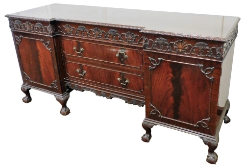 An early 20thC Adam style mahogany breakfront sideboard, with one long and two short fitted cushion drawers, carved with repeating scallop shells, Prince of Wales feathers and foliate scrolls, over two long drawers flanked by a pair of cupboard doors, the